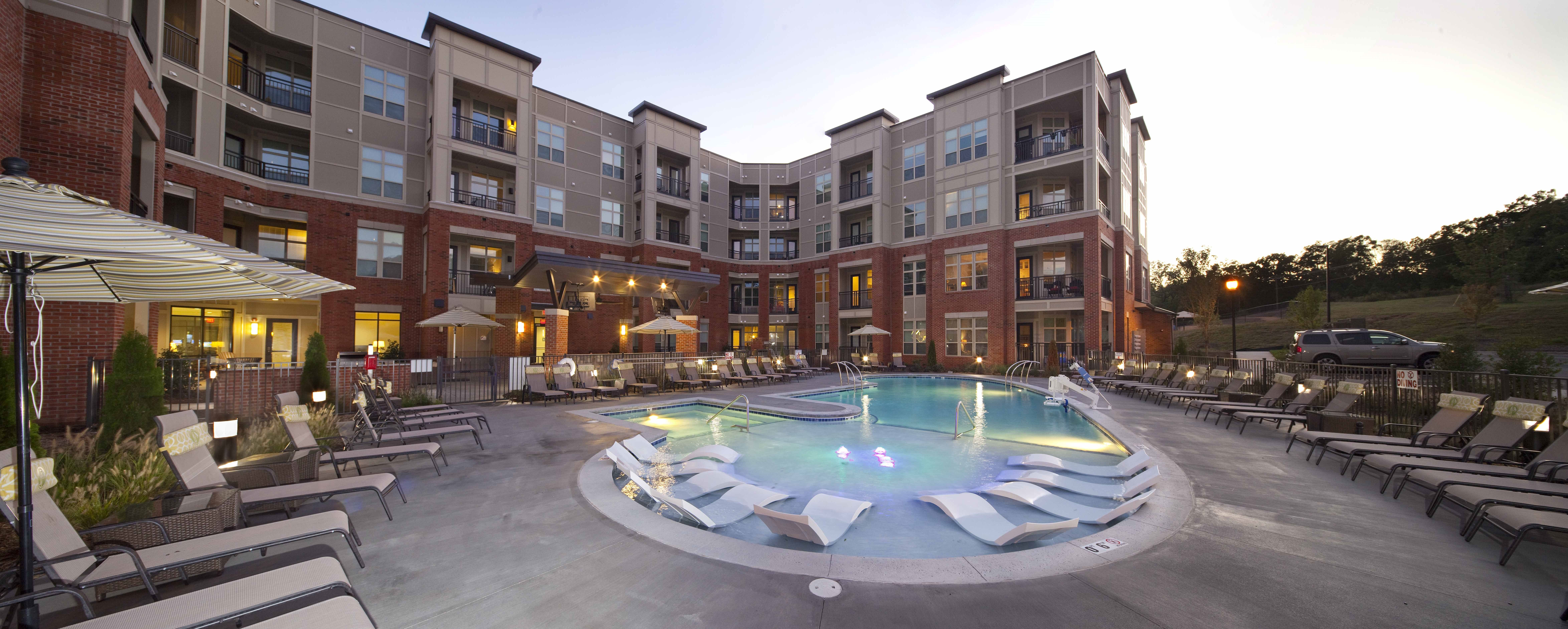 Apartments at Palladian Place in Durham, NC building exterior with saltwater pool, in-pool lounge chairs, and sitting area with chairs and umbrellas