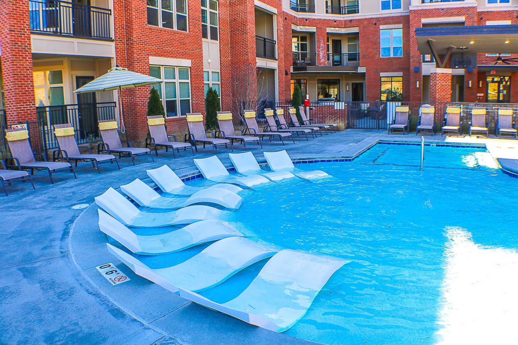 Apartments at Palladian Place in Durham, NC building exterior with saltwater pool, in-pool lounge chairs, and sitting area with chairs and umbrellas