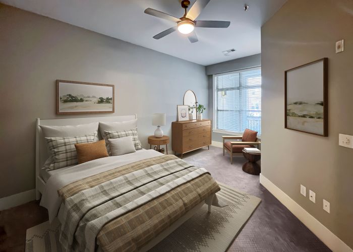 Apartments at Palladian Place in Durham, NC bedroom with large bed, dresser, ceiling fan, rug, chair, and large window